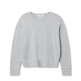 Woman wearing a light grey long-sleeve knit top with a relaxed fit, photographed against a soft neutral backdrop.