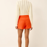 back of woman in white knit top and orange shorts on white background 