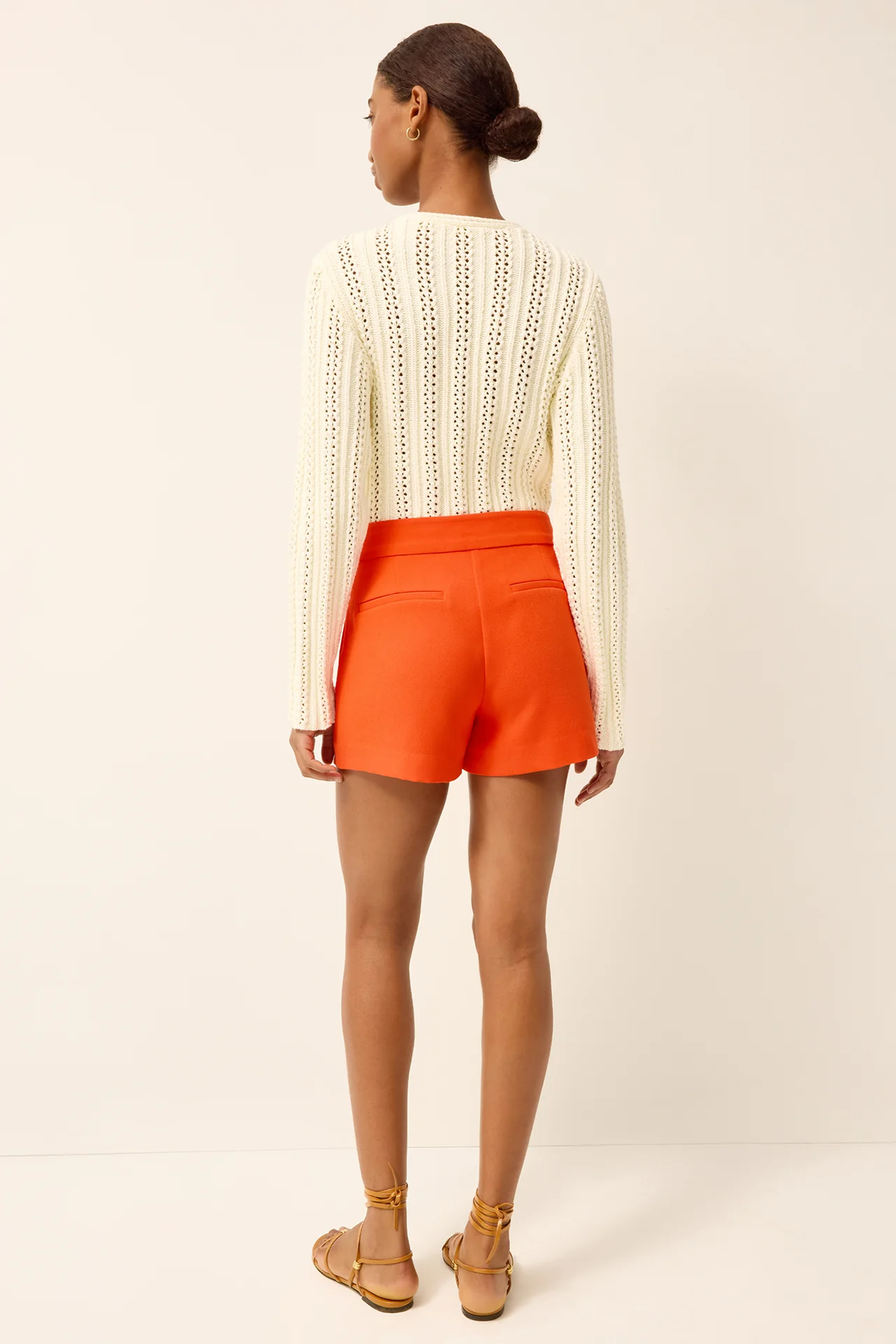 back of woman in white knit top and orange shorts on white background 