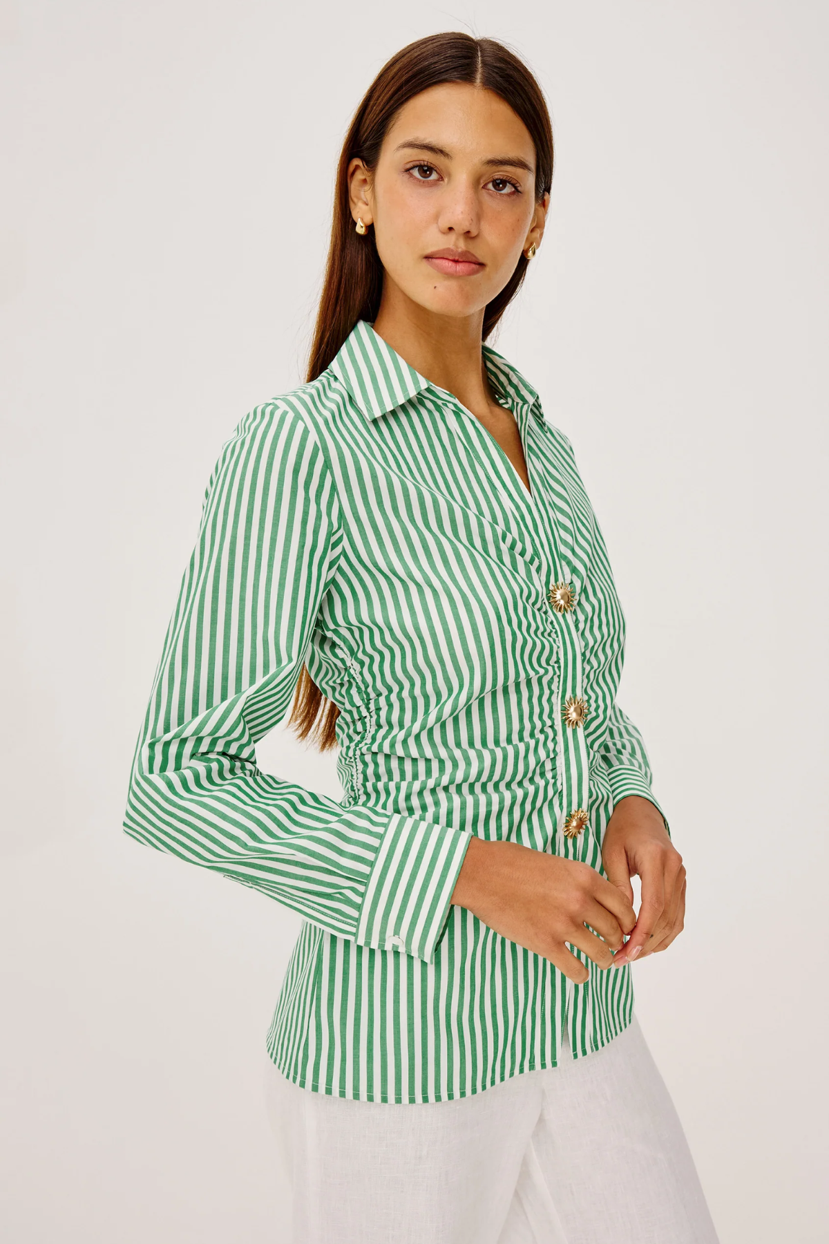 Woman wearing a green and white striped shirt with gold buttons on a white background
