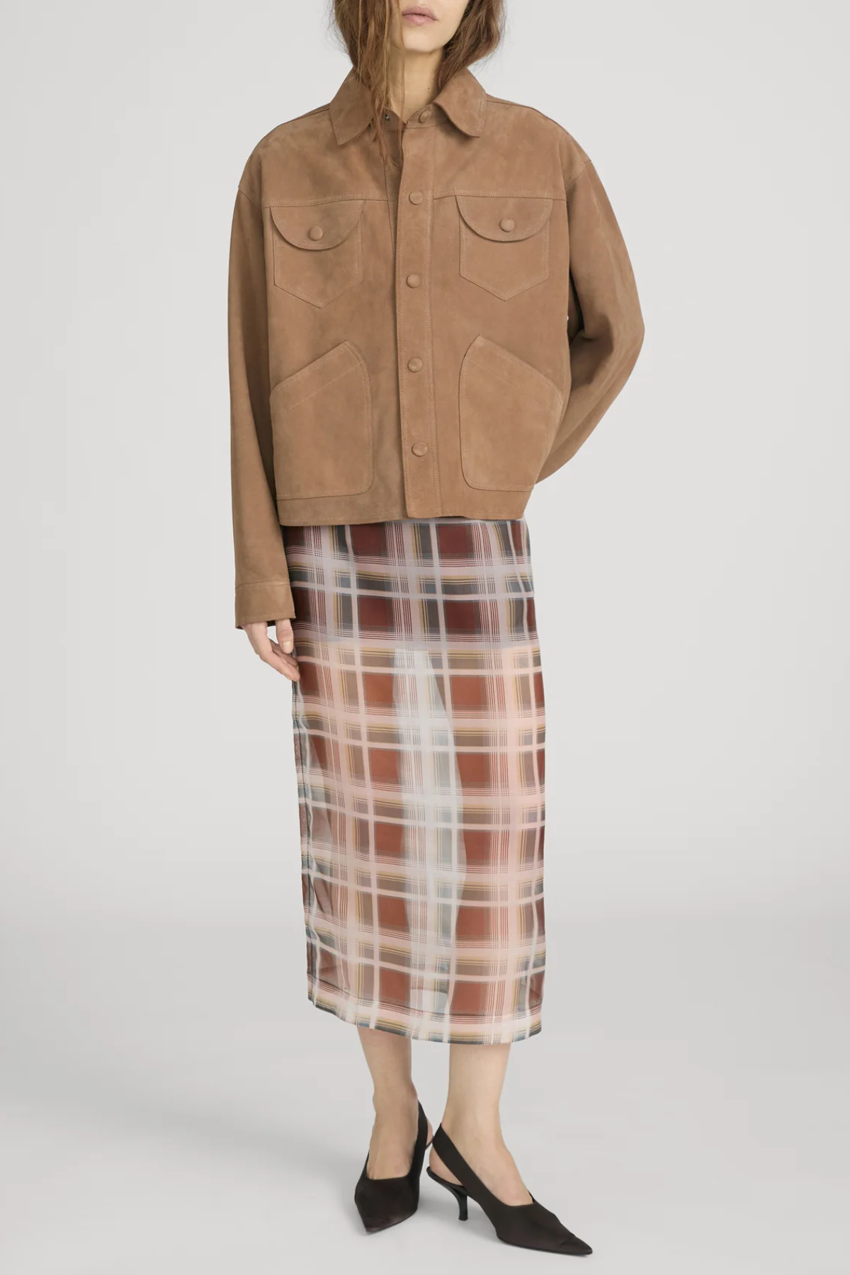 Person wearing a brown jacket and plaid skirt on a white background