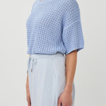Woman wearing a light blue textured top and light gray pants on a white background