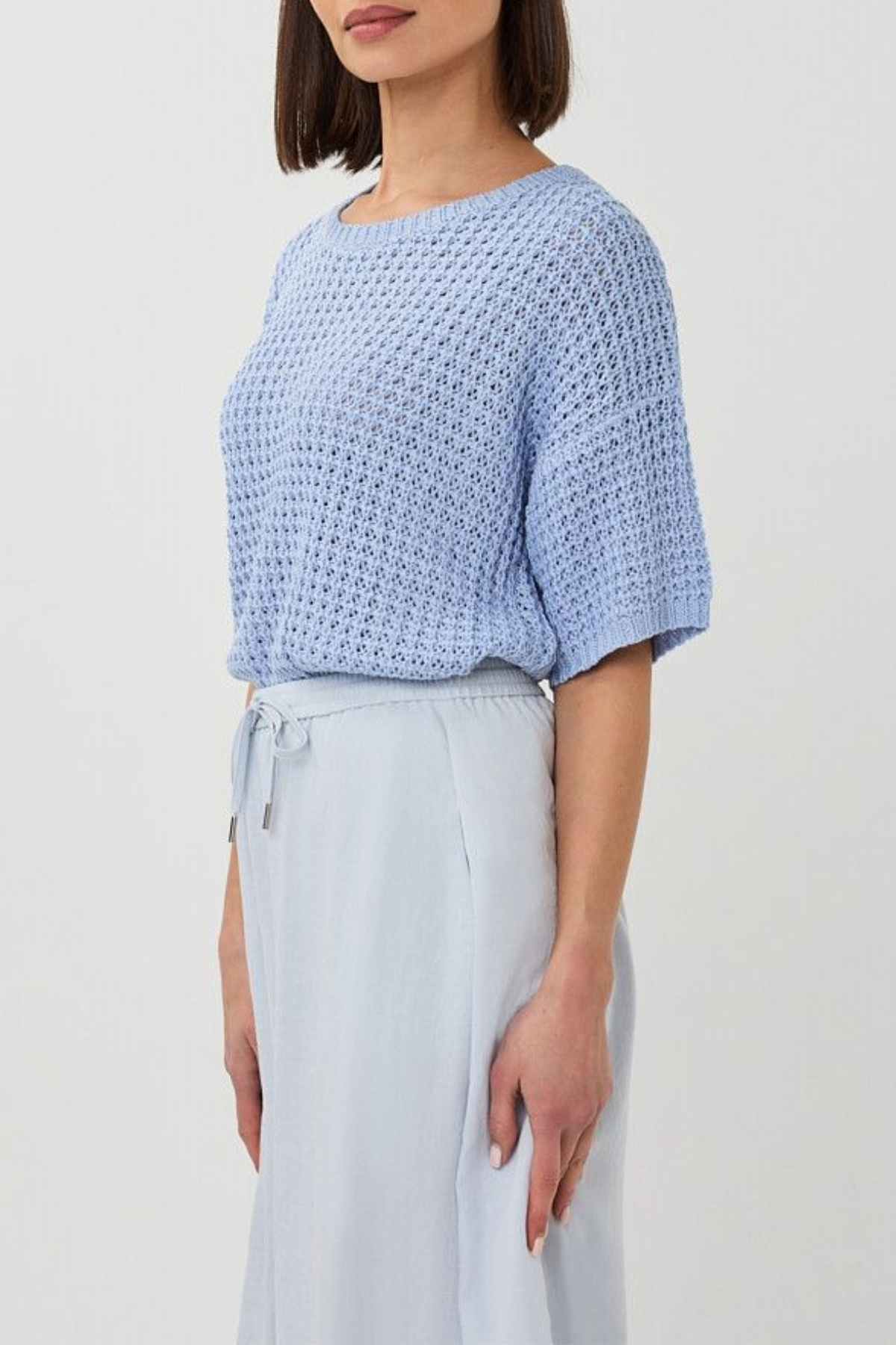 Woman wearing a light blue textured top and light gray pants on a white background