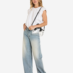 A woman modeling a white sleeveless top, light-wash wide-leg jeans, and black pointed-toe heels, carrying a small white crossbody bag with black studs and a black strap against a plain white studio background.