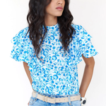 Woman wearing a blue floral top and jeans against a white background