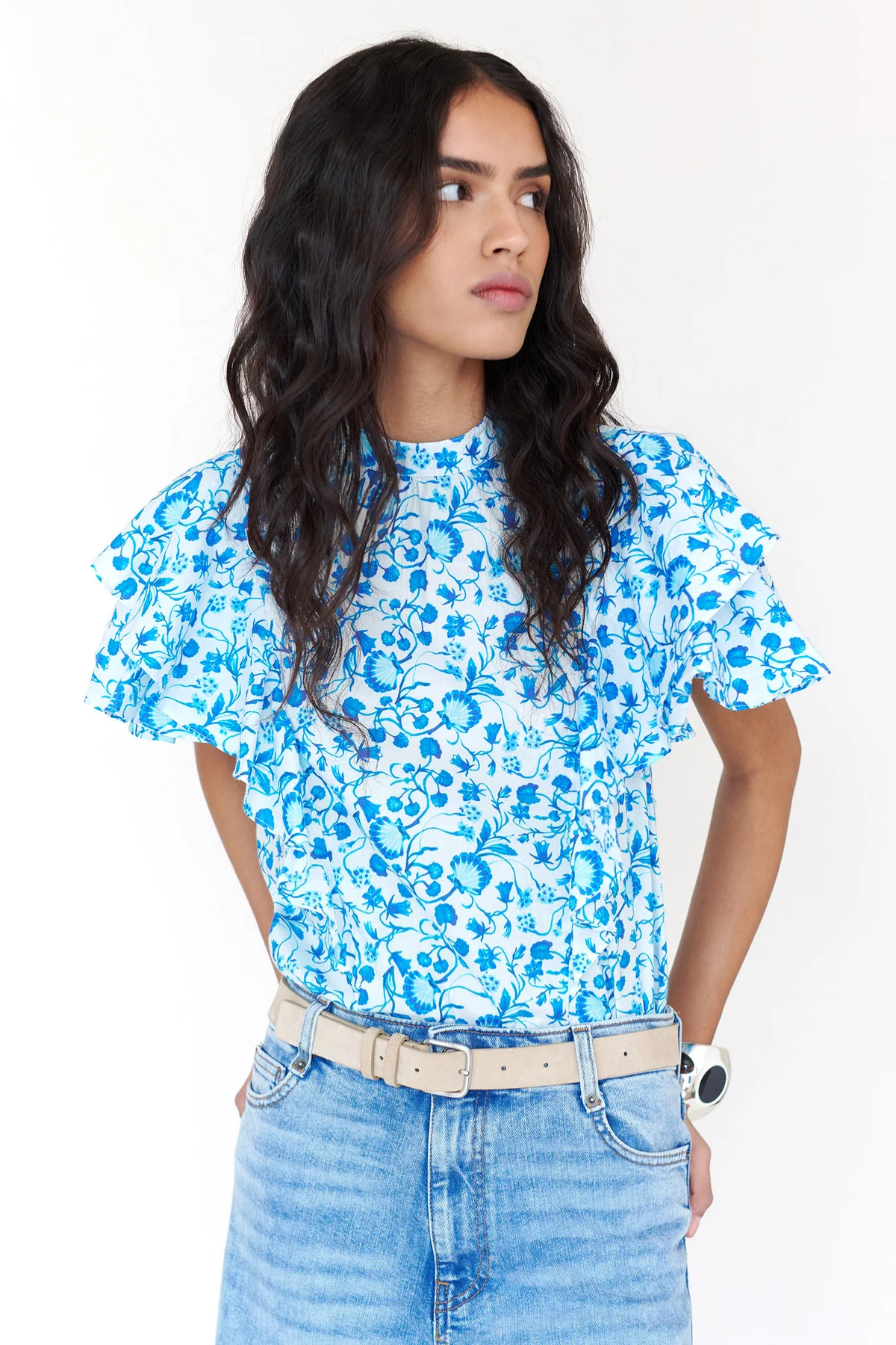 Woman wearing a blue floral top and jeans against a white background