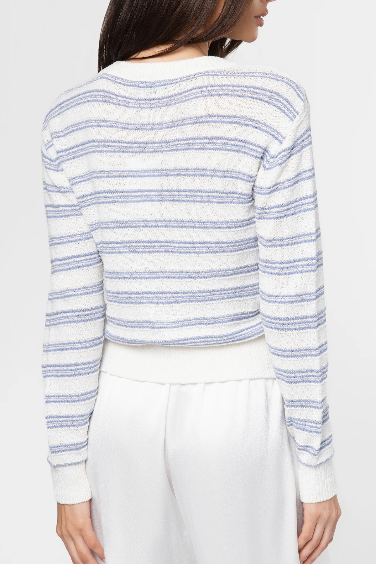 Person wearing a white and blue striped sweater with white pants on a light background