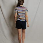 Person wearing a striped shirt and dark shorts standing against a plain white backdrop