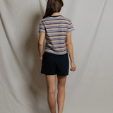 Person wearing a striped shirt and dark shorts standing against a plain white backdrop