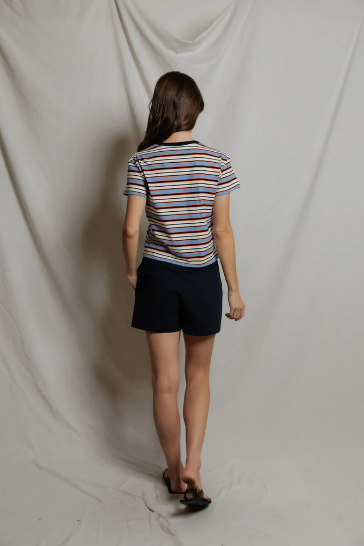Person wearing a striped shirt and dark shorts standing against a plain white backdrop