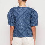 Person wearing a blue patterned top and white shorts on a plain background