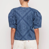 Person wearing a blue patterned top and white shorts on a plain background