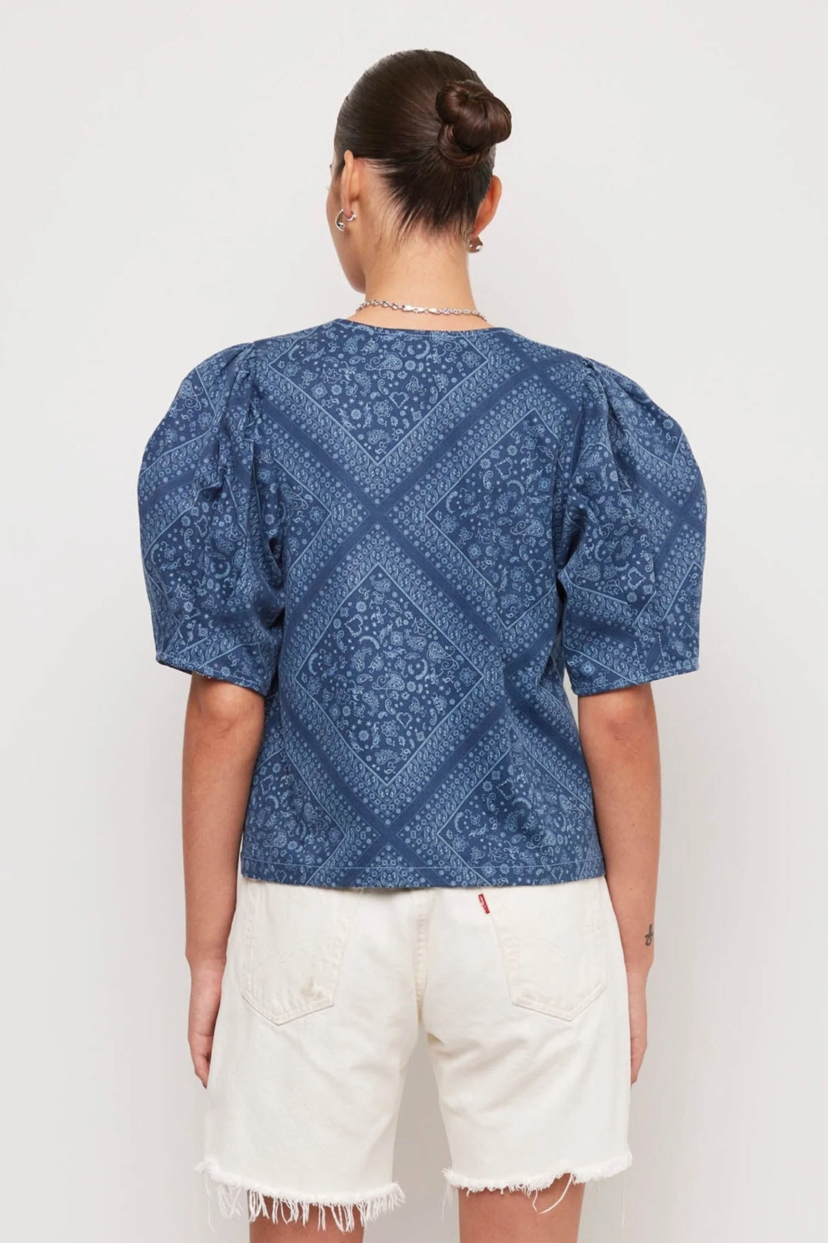 Person wearing a blue patterned top and white shorts on a plain background