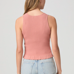Woman wearing a pink ribbed tank top and light blue jeans on a gray background