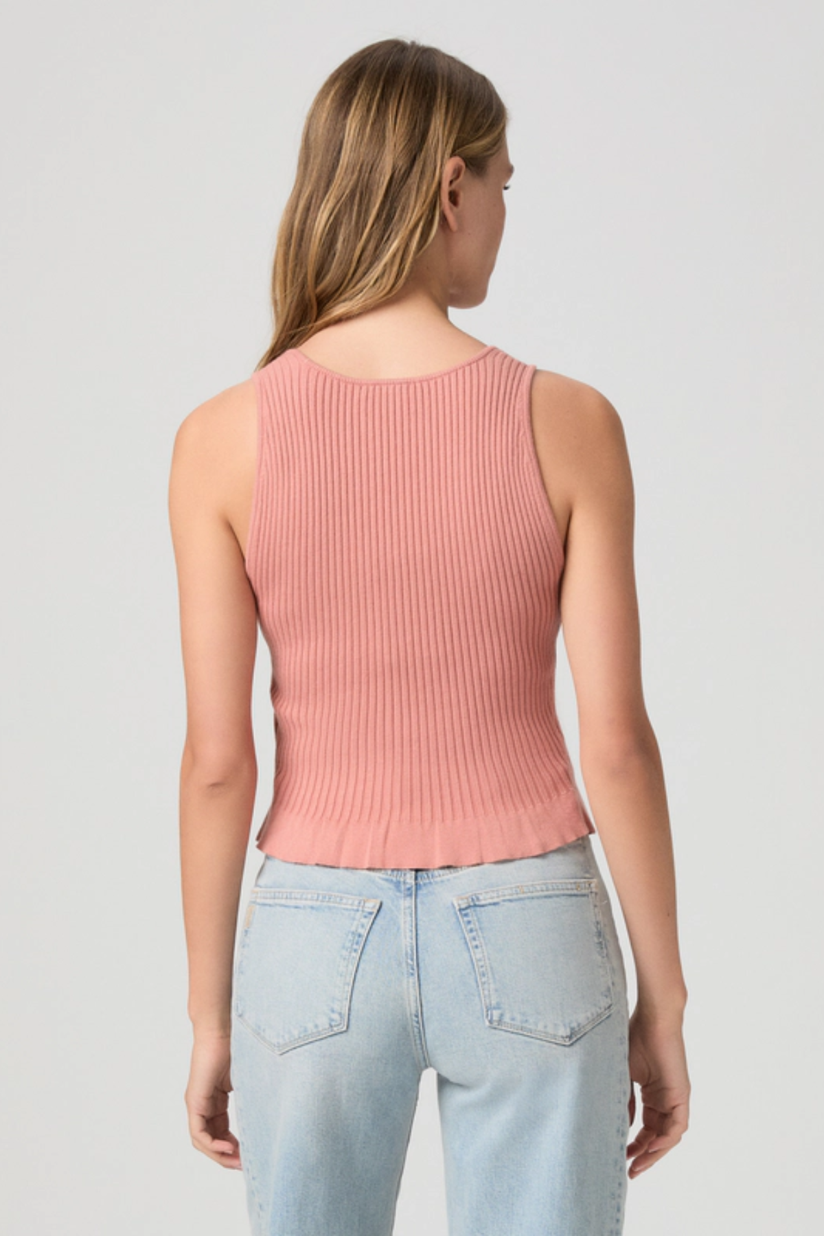 Woman wearing a pink ribbed tank top and light blue jeans on a gray background
