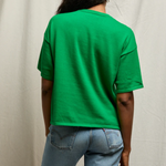 Person wearing a green t-shirt and blue jeans against a plain background