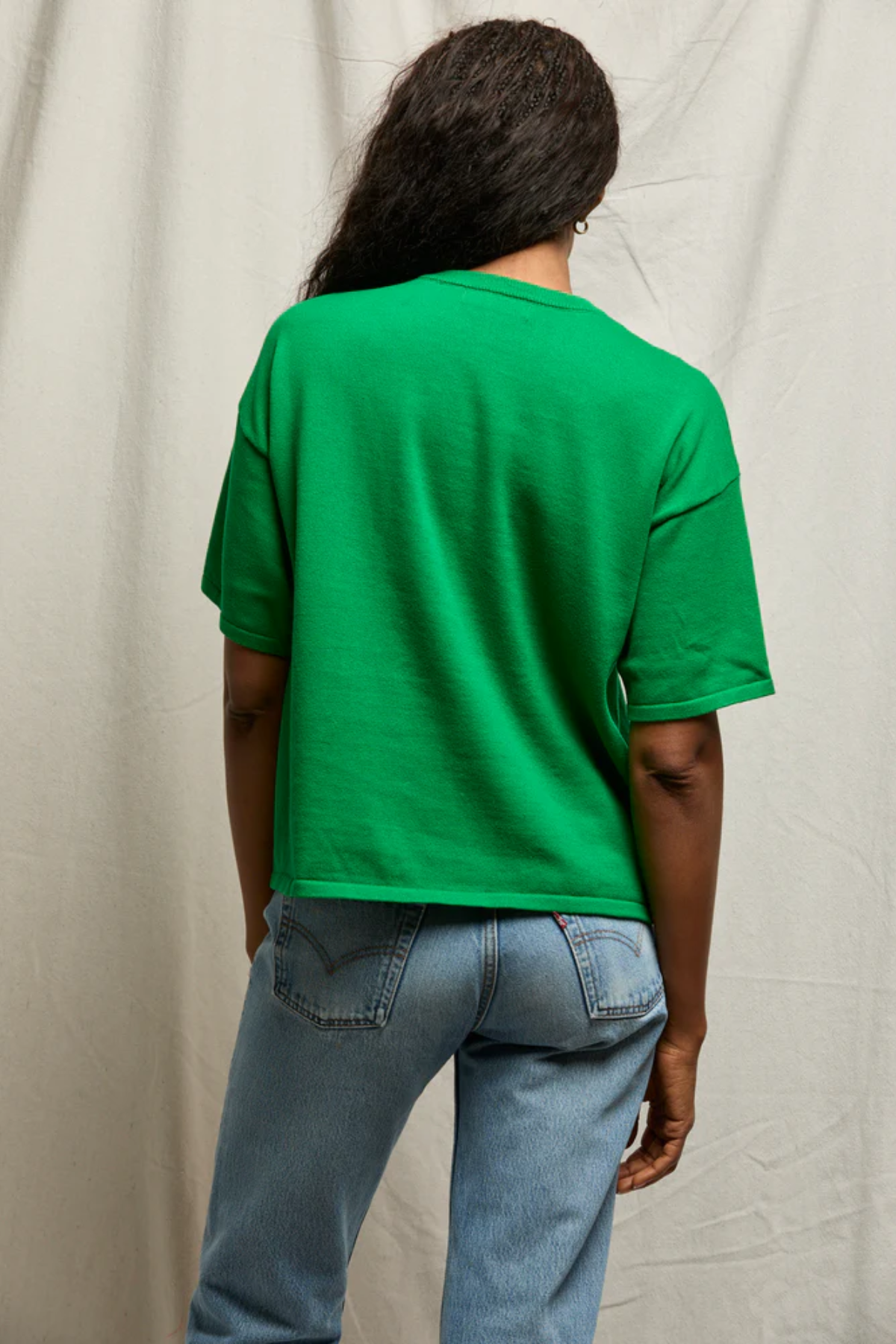 Person wearing a green t-shirt and blue jeans against a plain background