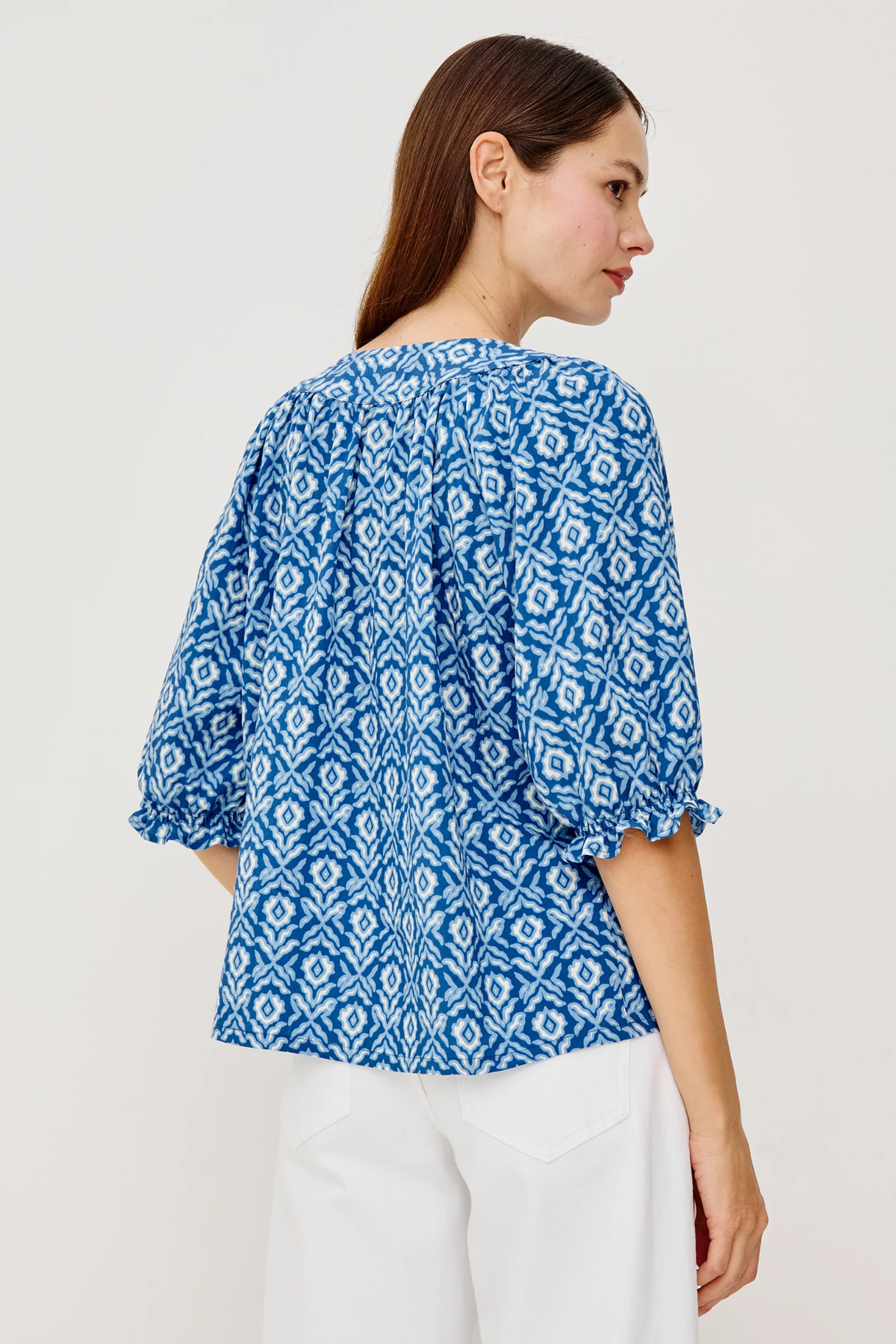 back of woman in blue printed blouse on white background 