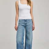Woman wearing a white tank top and blue jeans on a plain background