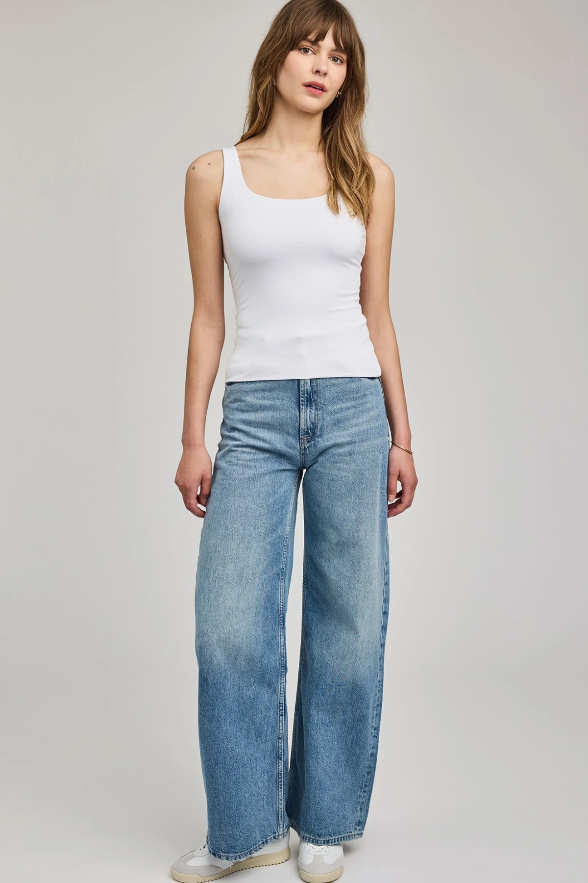 Woman wearing a white tank top and blue jeans on a plain background