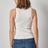 Woman wearing a white ribbed tank top with red trim and blue jeans on a gray background