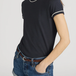 Person wearing a black t-shirt with white trim and denim shorts on a plain background
