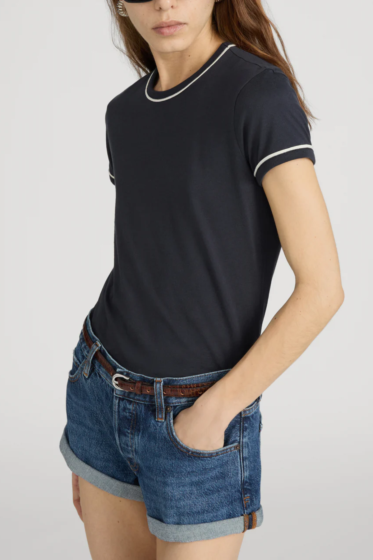 Person wearing a black t-shirt with white trim and denim shorts on a plain background