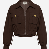 A dark brown cropped utility jacket with a front zipper, two flap pockets with gold-tone buttons, and drawstring details at the cuffs, shown on a light gray background.