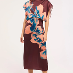 A woman modeling a sleeveless midi dress with a deep V-neckline, draped sheer cap sleeves, and a large floral print in peach and blue over a dark burgundy base, set against a plain white studio background.
