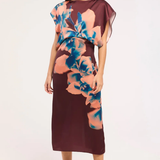 A woman modeling a sleeveless midi dress with a deep V-neckline, draped sheer cap sleeves, and a large floral print in peach and blue over a dark burgundy base, set against a plain white studio background.