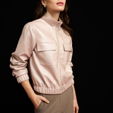 Woman wearing a light pink jacket and beige pants against a black background