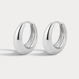 A pair of polished silver huggie hoop earrings with a smooth, rounded teardrop-like profile, displayed on a clean light gray background.