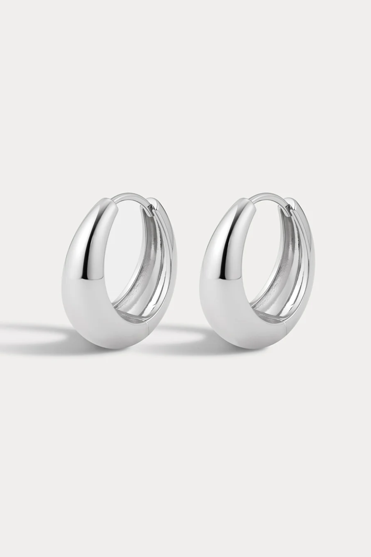 A pair of polished silver huggie hoop earrings with a smooth, rounded teardrop-like profile, displayed on a clean light gray background.