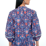 A woman shown from the back wearing a blue floral blouse with puff sleeves and light blue jeans against a plain white background.