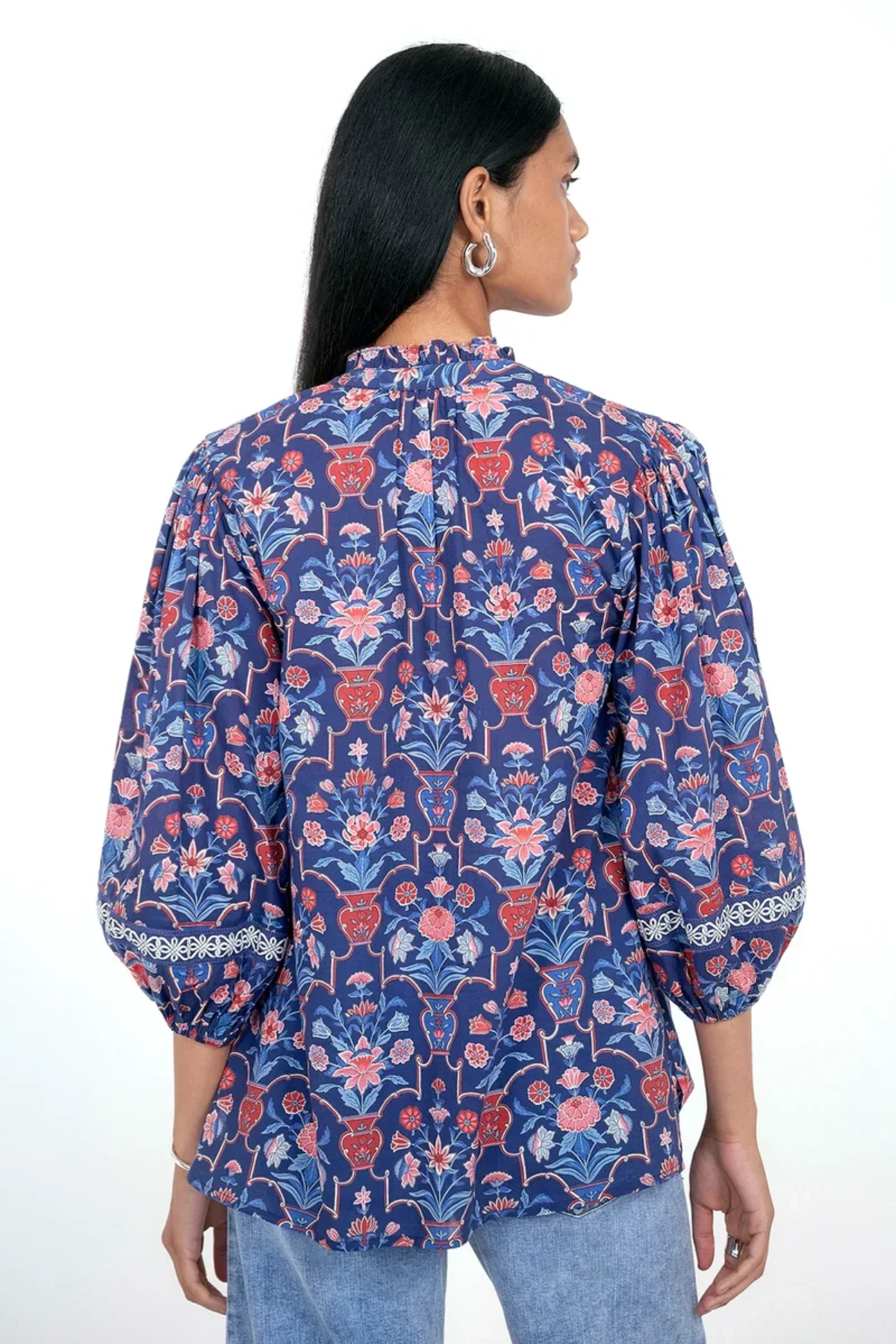 A woman shown from the back wearing a blue floral blouse with puff sleeves and light blue jeans against a plain white background.