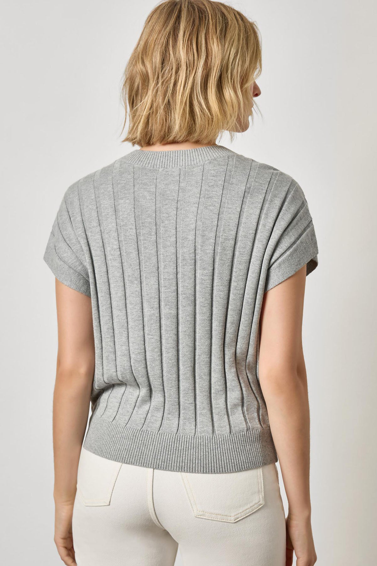 Person wearing a gray ribbed knit top against a white background