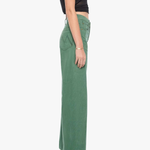 A side-profile view of a model wearing high-waisted, wide-leg sage green pants with a black sleeveless crop top and metallic high-heeled sandals, set against a plain white studio background.