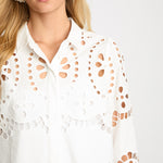 Woman wearing a white blouse with cut-out patterns on a plain background