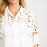 Woman wearing a white blouse with cut-out patterns on a plain background