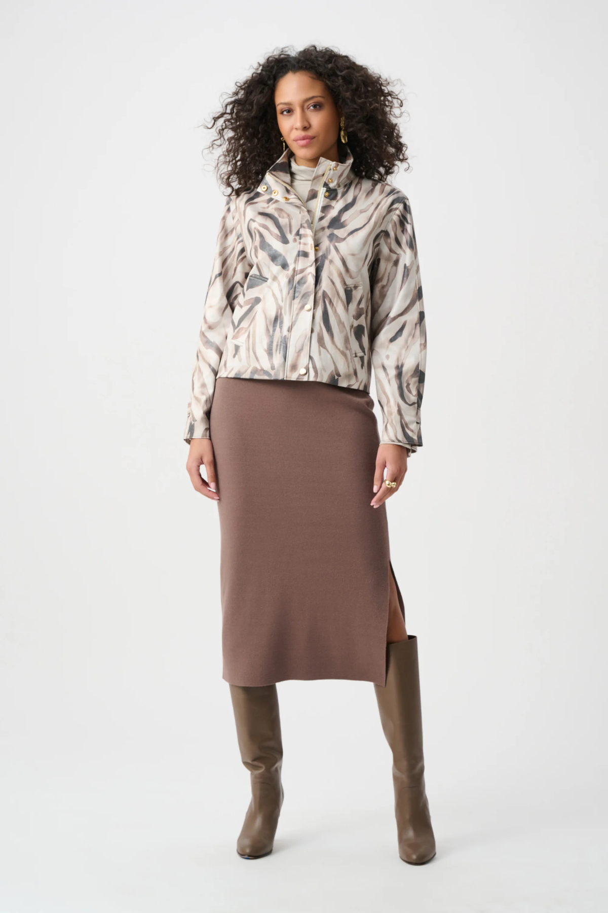 Woman wearing a patterned jacket, brown skirt, and brown boots on a white background