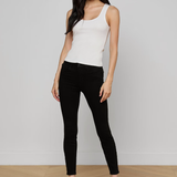 Woman wearing a white sleeveless top and black pants on a plain background