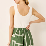 Woman wearing a white sleeveless top and green shorts with geometric pattern on a beige background