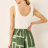 Woman wearing a white sleeveless top and green shorts with geometric pattern on a beige background