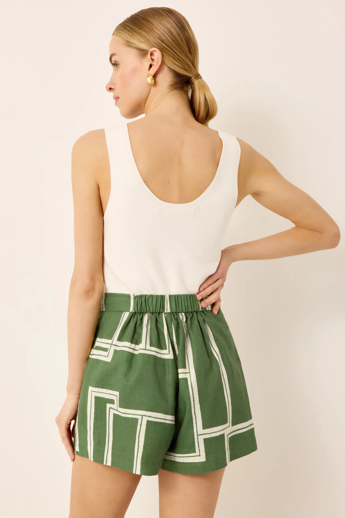 Woman wearing a white sleeveless top and green shorts with geometric pattern on a beige background