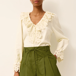 Woman wearing a white blouse with lace details and green shorts on a plain background