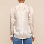 Person wearing a cream satin shirt and blue jeans against a beige background