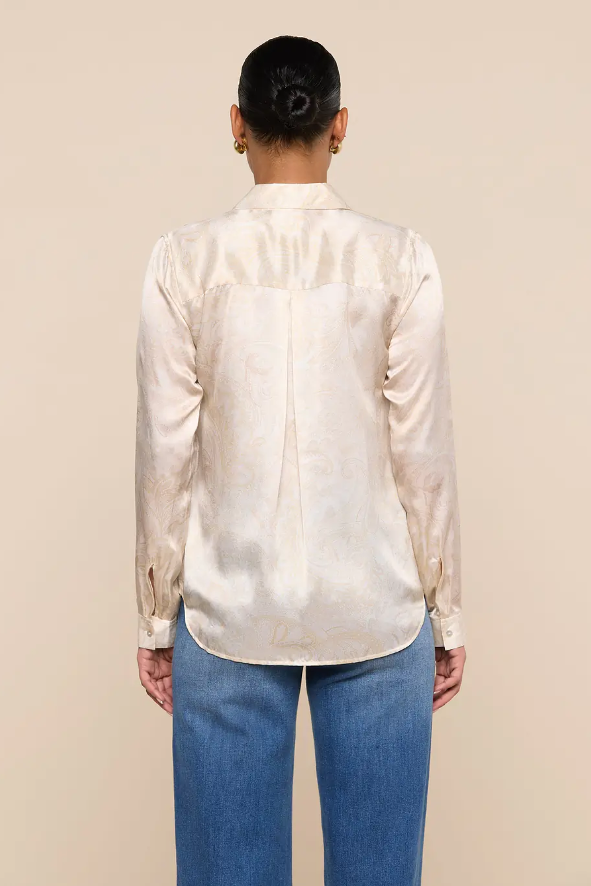 Person wearing a cream satin shirt and blue jeans against a beige background