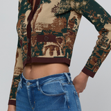 A cropped long-sleeve button-front top with a scenic landscape print in beige, brown, and dark green, worn by a model with blue jeans against a light gray studio background.