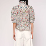 Person wearing a floral blouse and white pants on a plain background