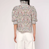 Person wearing a floral blouse and white pants on a plain background